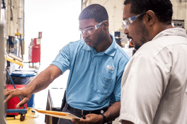 Two workers review a quality board in a plastic parts facility. 